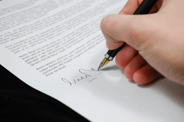 A person using a fountain pen to sign a contract, symbolizing the legal implications of Database Breaches.