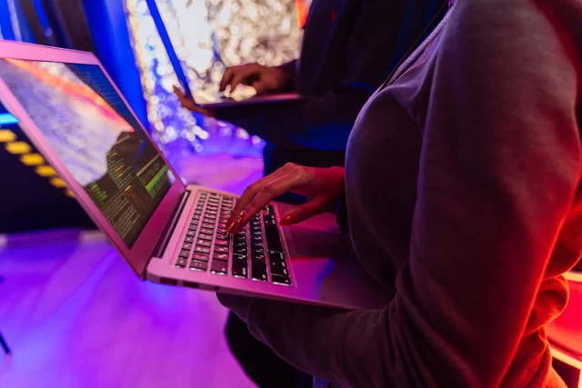 A close-up of a professional typing on a laptop displaying code in a neon-lit environment, representing the technical analysis of data flows required for a Data Protection Impact Assessment (DPIA)
