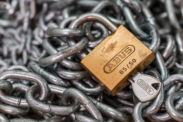 Brass padlock with a key inserted in a pile of iron chains, symbolizing protection against Security Breaches.
