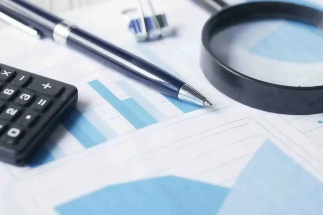 Calculator, pen, and magnifying glass resting on a graph, illustrating financial analysis for the payment card industry.