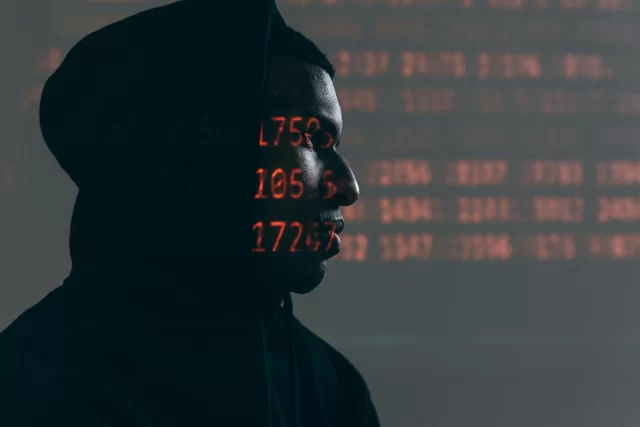 Profile of a person in a hoodie with red digital code projected onto their face, representing A Data Breach.